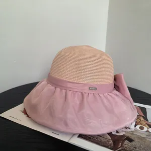 Detail of a beige straw hat with a pink organza bow and branded metal tag on a magazine