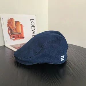 Détail d'une casquette plate en denim bleu foncé avec trois rayures blanches sur tissu texturé