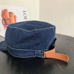 Détail de la casquette plate en denim avec coutures contrastées et lanière en cuir réglable