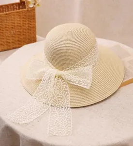 Close-up of a beige straw sun hat featuring an elegant white lace bow on white linen