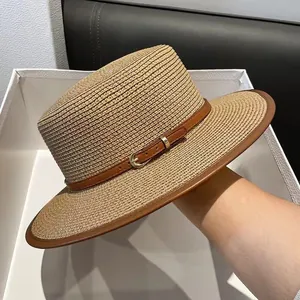 Close-up of woven straw sun hat featuring brown leather piping and metal buckle detail