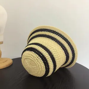 Dettaglio del cappello di paglia a righe nere e beige su un tavolo di legno scuro