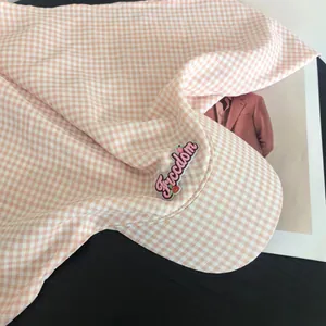 Dettaglio del cappellino a scacchi rosa con scritta freedom e ricamo a fragola
