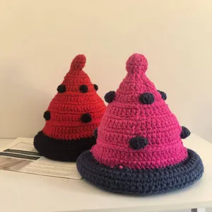 Detail of handmade knit pointed beanies with decorative pom-poms in red and pink colors