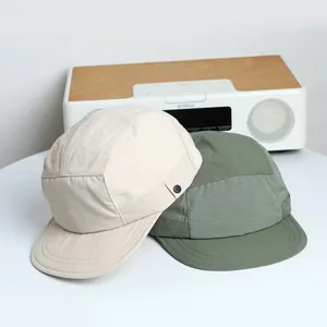Flat brim five-panel camper hats in beige and olive ripstop fabric on a white desk