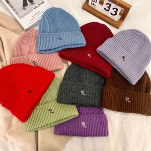 Winter knit beanies with embroidered R letter in various colors on a soft bed setting