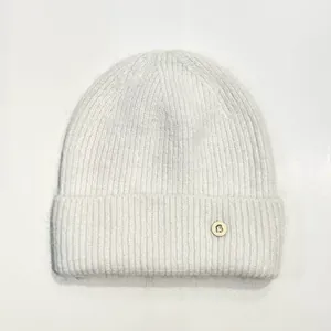 Detalle del gorro de punto de conejo blanco con un botón metálico decorativo letra B