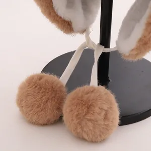 Detail of plush winter hat featuring soft camel faux fur with white fleece lining and pom-poms