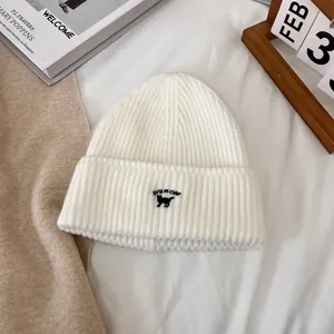Detalle del gorro de punto blanco con bordado de gato negro y letras decorativas