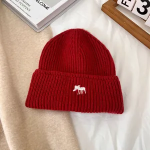 Primer plano de un gorro de punto rojo con bordado de alce blanco sobre un fondo acogedor