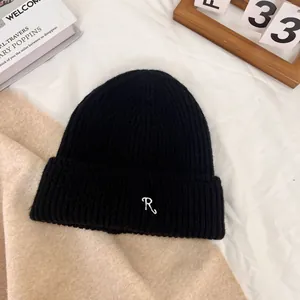 Close-up of black ribbed knit beanie with white R letter embroidery on a textured background
