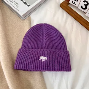 Primer plano de un gorro de punto morado con bordado de alce blanco en tela de canalé
