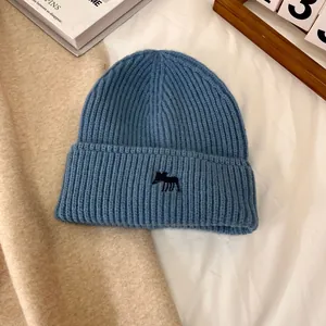 Detalle del gorro de punto azul marino con un pequeño bordado de animal negro