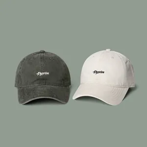 Detail of embroidered lettering on cotton baseball caps in charcoal and cream colors