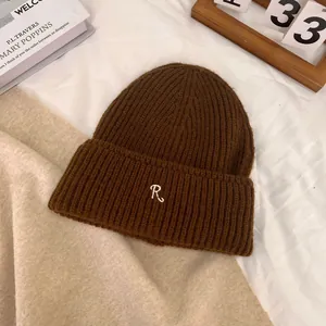 Detail of dark brown ribbed knit beanie with white embroidered letter R on the fold