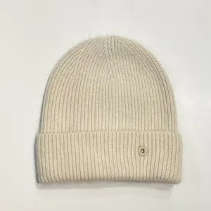 Detalle del tejido de punto acanalado y botón metálico con la letra B en un gorro crema