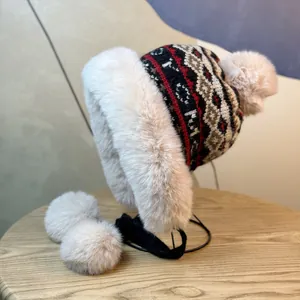 Detailed knit trapper hat showing white faux fur lining and plush pom-poms on wood table