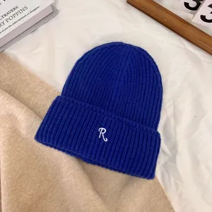 Detail of royal blue ribbed knit beanie with white embroidered letter R on white fabric