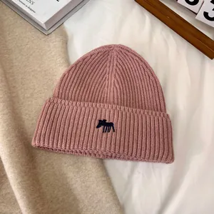 Vista macro del gorro de punto rosa loto con textura de canalé y bordado de alce