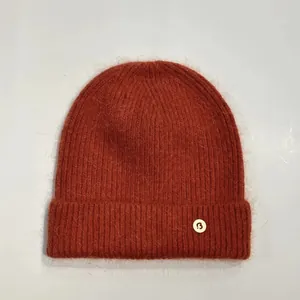 Detalle de gorro de punto de pelo de conejo naranja suave con insignia de la letra 'B'