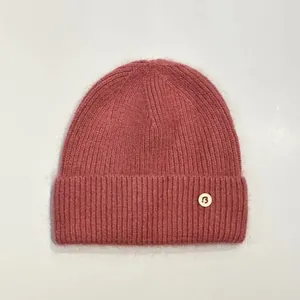 Detalle de gorro de punto de conejo rosa con insignia de la letra B y textura de canalé