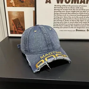 Detail of distressed brim on washed blue denim baseball cap with yellow MADTIME embroidery
