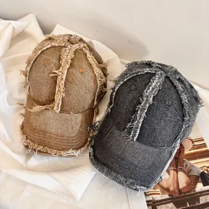 Distressed denim baseball caps with frayed edges in tan and charcoal grey on white fabric