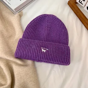 Detalle del tejido de un gorro morado con bordado de gato sobre fondo acogedor