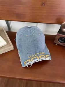 Detail of light blue washed denim baseball cap with yellow MADTIME embroidery and distressed brim