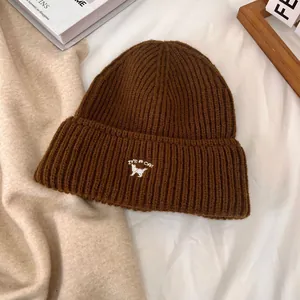 Detalle de gorro de punto marrón con bordado de gato blanco y frase It's a Cat