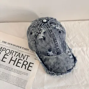 Detail of acid wash denim baseball cap featuring distressed holes and frayed edge design