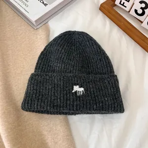 Detalle del gorro de punto gris oscuro con bordado de alce blanco en tejido grueso