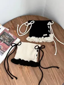 Détail du gilet en maille avec nœuds latéraux et ourlet à volants sur table en bois
