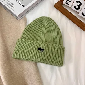 Detalle de gorro de punto verde con textura acanalada y bordado de un animal pequeño