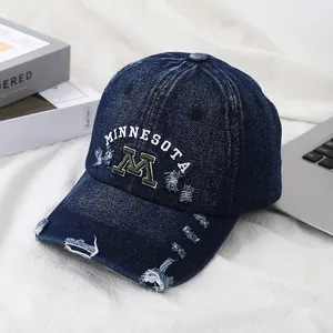 Detailed close-up of distressed denim baseball cap with vintage M letter embroidery