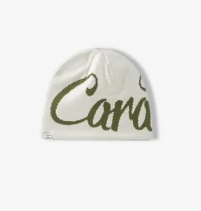 Detail of cream knit beanie with green jacquard lettering and stitched design label