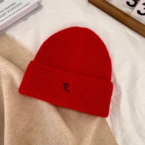 Detail of red knit beanie with black R letter embroidery on a warm textured background