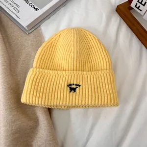 Detalle del gorro de punto amarillo con bordado de gato y letras negras decorativas