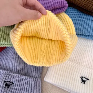 Detalle del tejido de punto acanalado y bordado de gato en gorros de invierno