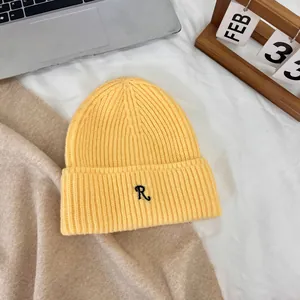 Detail of a bright yellow knitted beanie with a black embroidered letter R on the cuff