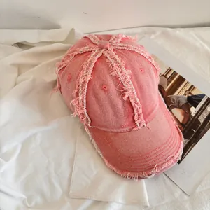 Close-up of pink denim baseball cap featuring vintage distressed frayed edges and washed texture