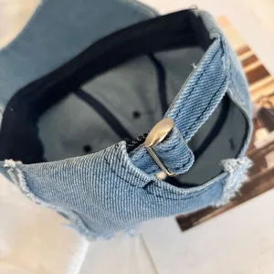 Close-up of light blue denim baseball cap with silver metal buckle and distressed frayed edges