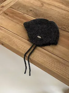 Close-up of charcoal grey wool beanie with metal logo tag and drawstrings on wood