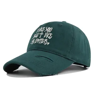 Close-up of white letter embroidery and distressed brim on a dark green cotton baseball cap