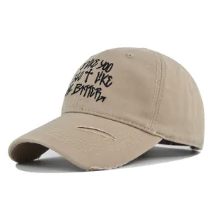 Close-up of khaki baseball cap featuring distressed brim and black graffiti text embroidery