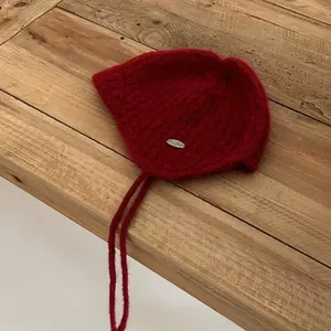 Detail of red mohair knit hat with ear flaps, metal logo tag and braided ties on wood