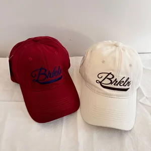 Detail of red and beige baseball caps featuring Brkln embroidery and stiff cotton texture