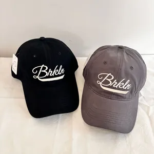 Detail view of black and dark grey baseball caps with Brkln embroidery on white fabric