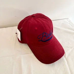 Close-up of deep red baseball cap with blue embroidery and white brand tag details