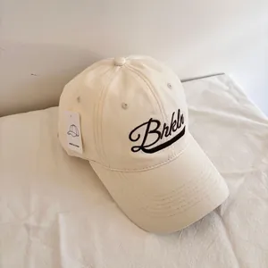 Detailed view of beige baseball cap with black Brkln embroidery and white paper hang tag